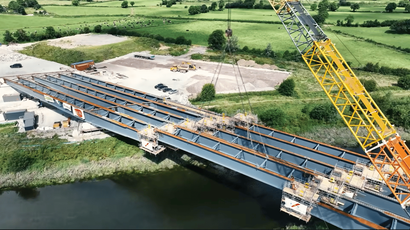 Steel bridge under construction over a river, with a crane lifting girders